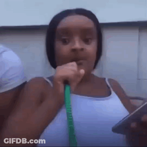 A Woman In A White Tank Top Is Holding A Green Hose In Her Mouth . GIF