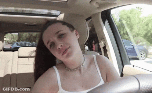 A Woman In A White Tank Top Is Sitting In A Car GIF
