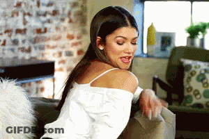 A Woman In A White Tank Top Is Sitting On A Couch With Her Tongue Out . GIF