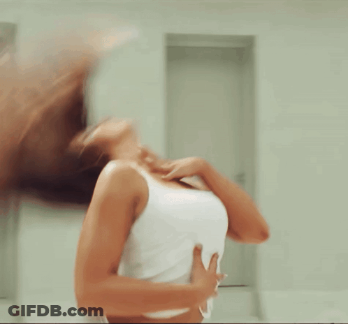 A Woman In A White Tank Top Is Standing In A Room GIF