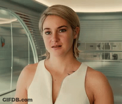 A Woman In A White Tank Top Is Standing In A Room Looking At The Camera . GIF