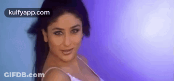 A Woman In A White Tank Top Is Standing In Front Of A Blue Wall . GIF