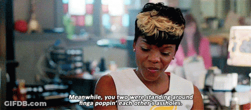 A Woman In A White Tank Top Is Standing In Front Of A Computer And Talking To Another Woman . GIF