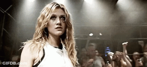 A Woman In A White Tank Top Is Standing In Front Of A Crowd Of People . GIF
