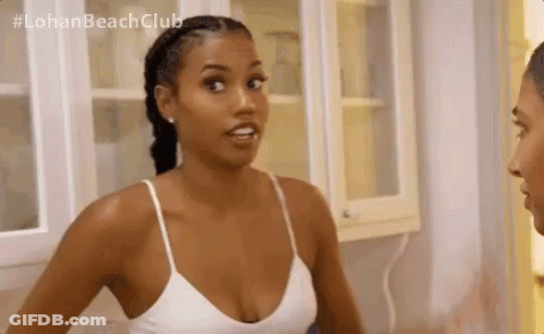 A Woman In A White Tank Top Is Standing Next To A Man In A Kitchen And Talking To Him . GIF