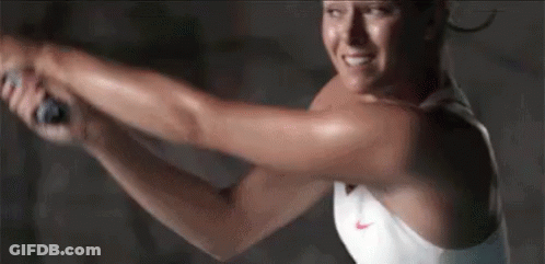 A Woman In A White Tank Top Is Swinging A Tennis Racquet . GIF