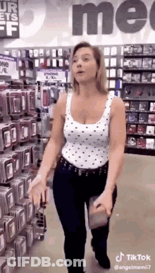 A Woman In A White Tank Top Is Walking Through A Store Holding A Cell Phone Case . GIF
