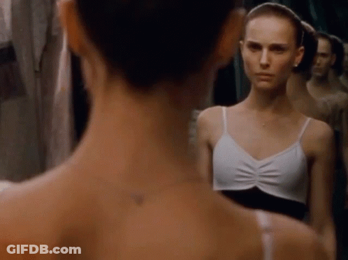 A Woman In A White Tank Top Looks At Her Reflection In A Mirror GIF