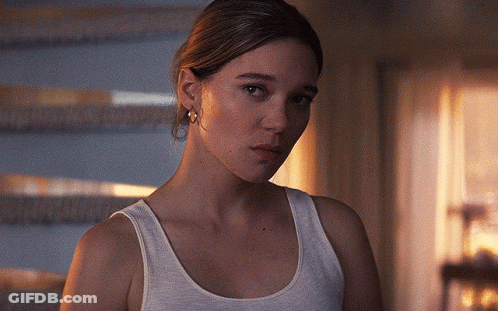 A Woman In A White Tank Top Looks At The Camera With A Serious Look On Her Face GIF