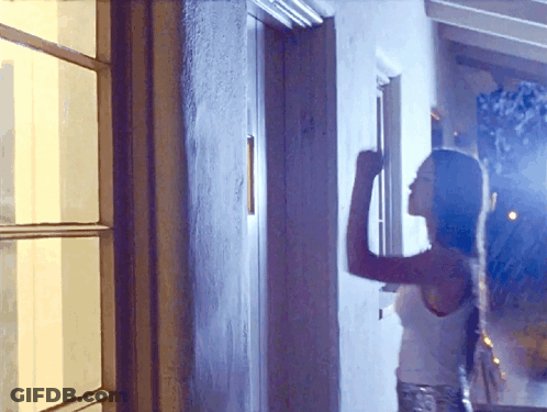 A Woman In A White Tank Top Stands In Front Of A Window GIF
