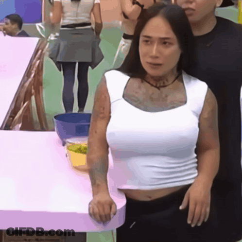 A Woman In A White Tank Top Stands Next To A Man GIF
