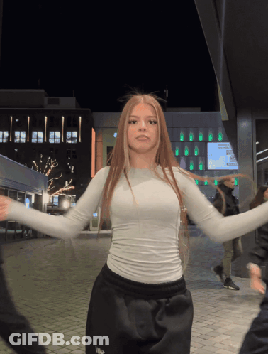 A Woman In A White Top Is Dancing In Front Of A Building GIF