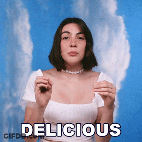A Woman In A White Top Is Holding A Piece Of Paper With The Word Delicious Written On It GIF