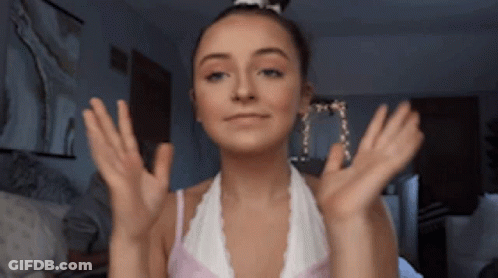 A Woman In A White Top Is Making A Face With Her Hands Outstretched GIF