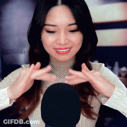 A Woman In A White Top Is Smiling And Holding Her Hands Up In Front Of A Microphone GIF