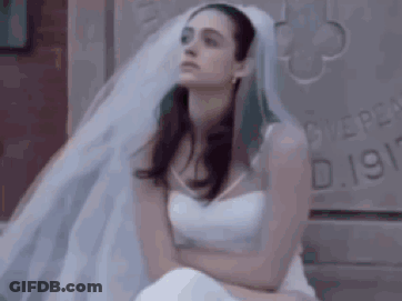 A Woman In A White Wedding Dress And Veil Is Sitting On A Bed . GIF