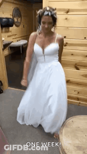 A Woman In A White Wedding Dress Is Dancing In A Room With A Wooden Wall . GIF