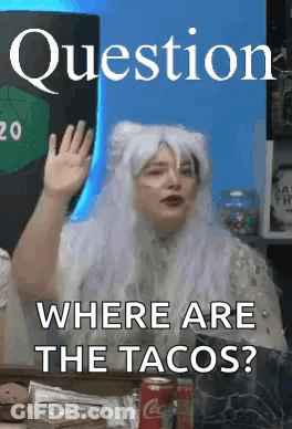 A Woman In A White Wig Is Sitting At A Table Waving Her Hand . GIF