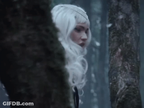 A Woman In A White Wig Is Standing In A Dark Forest GIF
