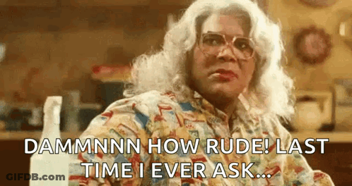 A Woman In A Wig And Glasses Is Sitting At A Table With A Spray Bottle In The Background . GIF