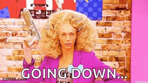A Woman In A Wig Is Holding A Gun In Front Of A Brick Wall And Says `` Going Down '' . GIF
