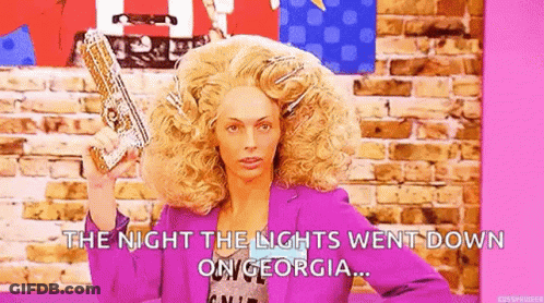 A Woman In A Wig Is Holding A Gun In Her Hand . GIF