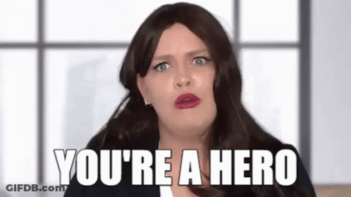 A Woman In A Wig Is Saying `` You 'Re A Hero '' While Making A Funny Face . GIF