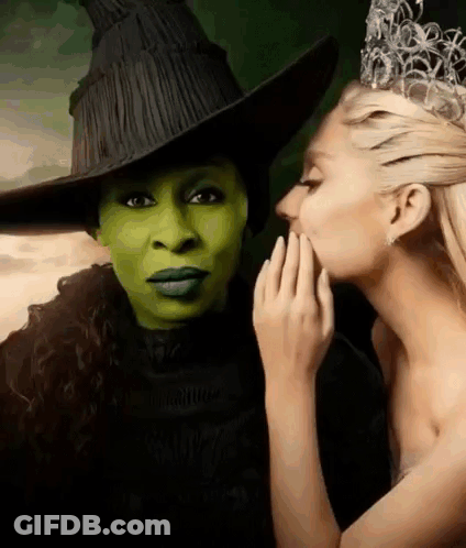 A Woman In A Witch Costume Is Whispering Into The Ear Of Another Woman In A Crown . GIF