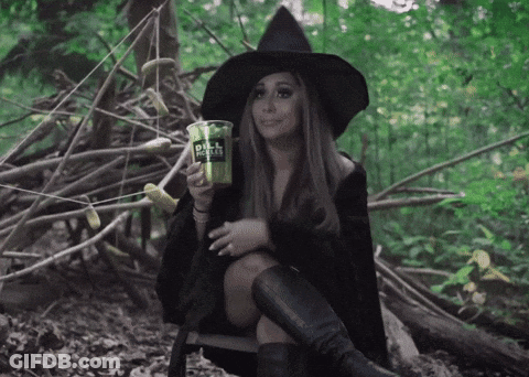 A Woman In A Witch Costume Sits In The Woods Holding A Cup That Says Dill Coffee GIF