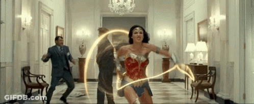 A Woman In A Wonder Woman Costume Is Holding A Lightning Bolt In A Hallway GIF