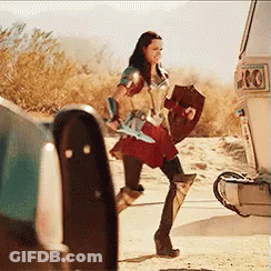 A Woman In A Wonder Woman Costume Is Holding A Shield And Sword While Walking Towards A Van . GIF