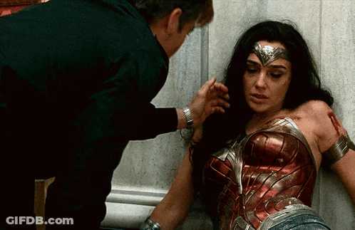A Woman In A Wonder Woman Costume Is Laying On The Ground While A Man Holds Her Arm . GIF