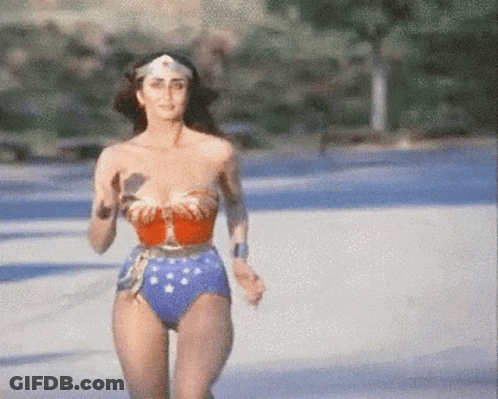 A Woman In A Wonder Woman Costume Is Running Across A Road . GIF
