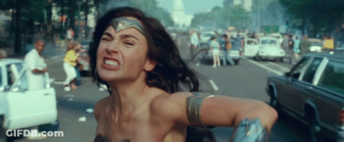 A Woman In A Wonder Woman Costume Is Running Down A Street With Cars . GIF