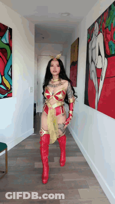 A Woman In A Wonder Woman Costume Is Standing In A Hallway Holding A Sword . GIF