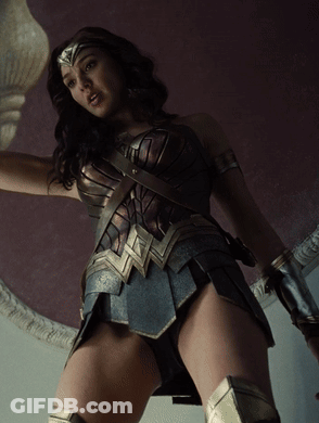 A Woman In A Wonder Woman Costume Is Standing In Front Of A Purple Wall GIF