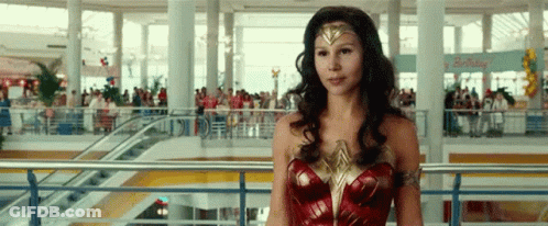 A Woman In A Wonder Woman Costume Is Standing On A Balcony In A Shopping Mall . GIF