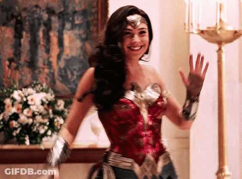 A Woman In A Wonder Woman Costume Is Waving Her Hand And Smiling . GIF