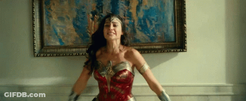 A Woman In A Wonder Woman Costume Stands In Front Of A Framed Picture GIF
