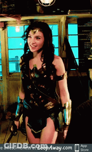 A Woman In A Wonder Woman Costume Stands In Front Of A Window GIF