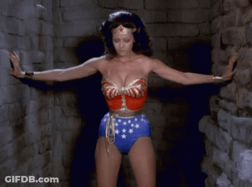 A Woman In A Wonder Woman Outfit Is Standing In A Dark Room GIF