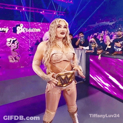 A Woman In A Wrestling Outfit Is Standing In Front Of A Purple Wall That Says Tiffanyluv24 GIF