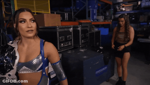 A Woman In A Wrestling Outfit Stands In Front Of A Blue Box That Says ' Warehouse ' On It GIF