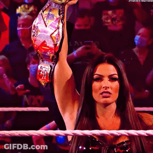 A Woman In A Wrestling Ring Holds A Championship Belt Over Her Head GIF