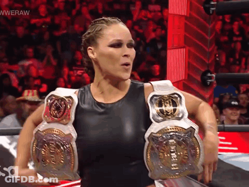 A Woman In A Wrestling Ring Is Holding A Belt That Says Wweraw GIF