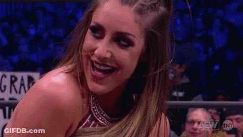 A Woman In A Wrestling Ring Is Smiling In Front Of A Crowd Of People . GIF