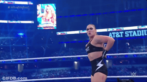A Woman In A Wrestling Ring With A Sign That Says At & T Stadium In The Background GIF