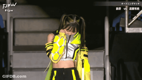 A Woman In A Yellow And Black Outfit With The Letters Tjpw On The Top GIF