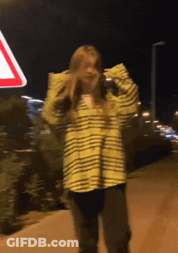 A Woman In A Yellow And Black Striped Shirt Is Standing In Front Of A Red And White Sign GIF