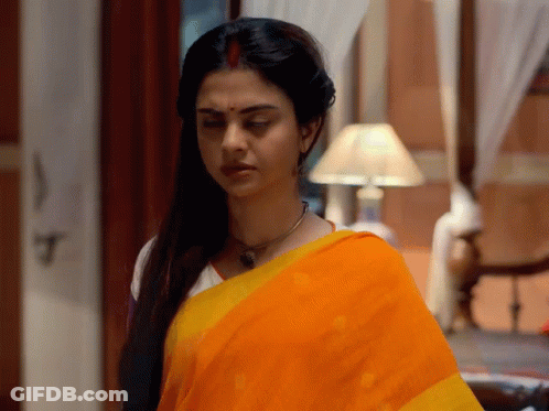 A Woman In A Yellow And Orange Saree Is Standing In A Room GIF